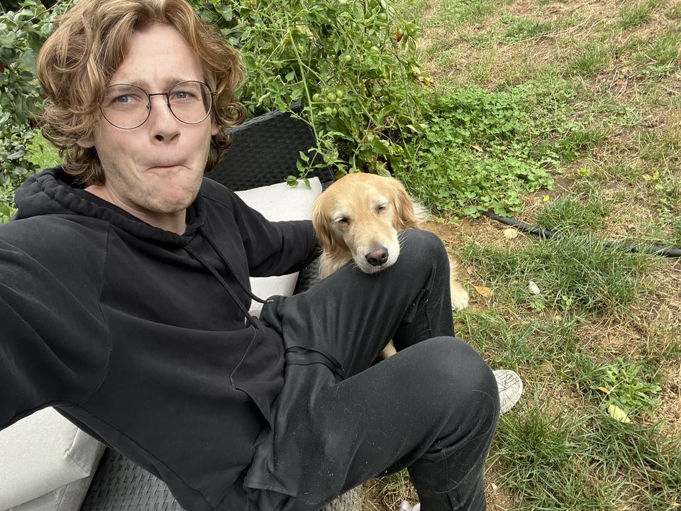 Caleb sitting outside with a golden retriever resting its head on his leg