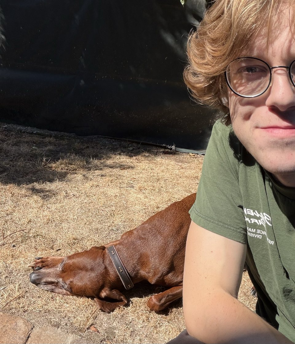 Caleb sitting beside a brown dog resting on the grass